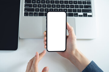 Blank white screen cell phone mockup. Close up, woman using smartphone on office table during working on laptop computer and digital tablet, empty space for social media marketing or mobile app design