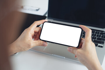 Blank white screen cell phone mockup. Close up, business woman using smartphone on office table during working on laptop computer, horizontal empty space for video marketing or mobile app design