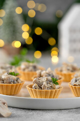 Christmas food. Mini tartlets with mushrooms in a cream sauce, with cheese, garlic and herbs on a white plate on a gray concrete background.