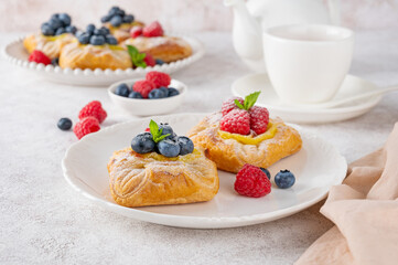 Danish puff pastry cakes with custard cream and fresh berries, sprinkled with powdered sugar on a white plate on a concrete background.