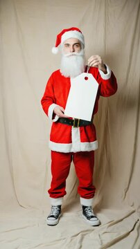 Santa Claus holding a blank white price tag, offering space for customizable sale or gift messages. E-commerce, discounts, or festive label
