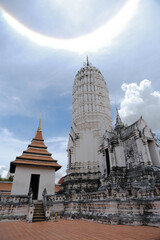 A white main prang in Khmer art and a Thai-style building, with a sun halo in the sky at Wat Phutthaisawan, Thailand.