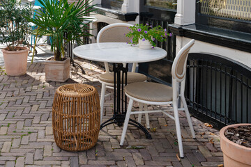 Outdoor cafe seating with marble table, chairs, stool, and potted plants on a brick patio.