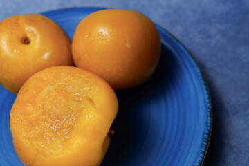 Round yellow plums on a blue plate, one cut open and revealing juicy pulp
