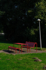 Red metal picnic set on a concrete pad by green grass and a sleek silver lamp post.