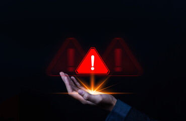 A hand holding a glowing red warning alert icon with an exclamation mark on dark background, symbolizing danger, risk, cybersecurity threat, or system error concept in technology and safety.