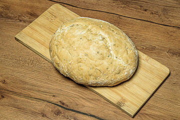 First-person view of round loaf of homemade rye bread placed on a wooden bamboo cutting board on a hardwood texture countertop. Baking concept, symbol of happy family life