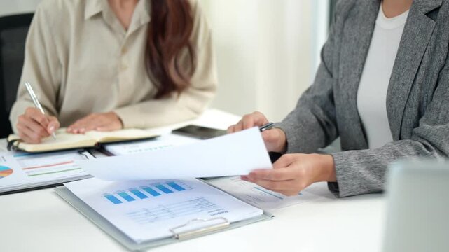 Asian adult businesswomen finance professionals collaborate analyze financial reports data using calculator documents strategic planning modern office setting business growth