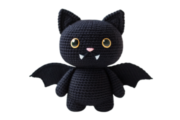 Crocheted black bat plush with golden eyes, pink nose, white fangs, fabric wings spread wide, isolated on a transparent background