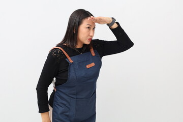 Side view portrait of a curious Asian woman in an apron, holding her hands over her eyes and...