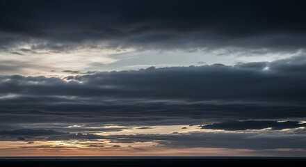 Dark, moody storm clouds gathering in the sky during sunset with hints of light