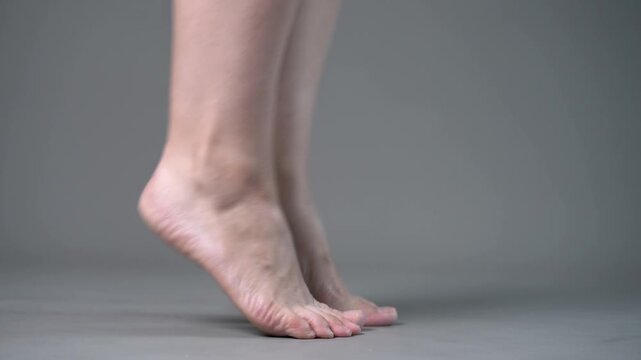 Individual leg training on a gray studio background, bare feet, demonstrating foot position and stability