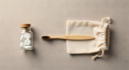 Top-down flatlay of bamboo toothbrush, glass jar, and cloth bag on beige background, sustainability stock concept
