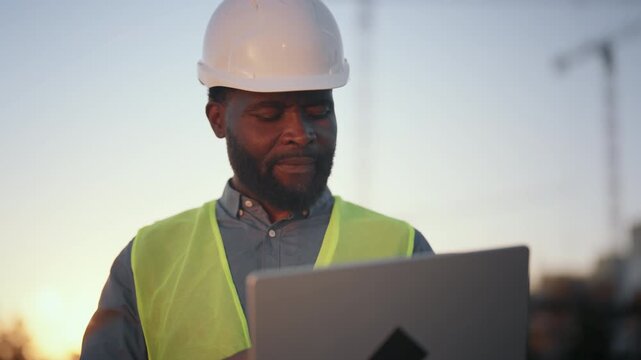 Medium portrait of high-skilled engineer with laptop at construction site. Innovation and modern technology in architecture and development, new software for builders and foreman, african american man - Powered by Adobe
