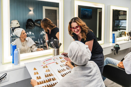 Hair stylist helping a woman wrapped in a towel choose a new hair color from a swatch book in a modern salon