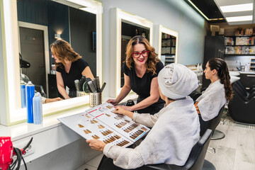 Hairdresser showing hair dye color chart to female client during consultation in modern beauty salon, choosing new color and treatment