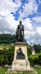Fototapeta premium Bronze statue atop plinth against lush greenery and cloudy sky