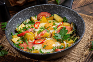 Fried eggs and potatoes, tomatoes, zucchini  and chili peppers on wooden table.