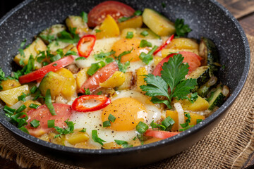 Fried eggs and potatoes, tomatoes, zucchini  and chili peppers on wooden background.