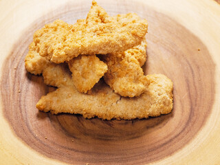 Uncooked chicken goujons or tenders on a wooden board. Popular classic chicken dish made from pieces of breast and breadcrumbs. Traditional ready to cook poultry product.