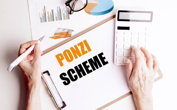 Clipboard with text ponzi scheme on white desk with charts, calculator, pen and hands holding stationery