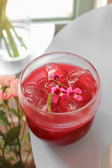 Vertical shot of iced Earl Grey mixed berry tea in a clear glass with ice cubes and pink floral detail, refreshing healthy summer cafe drink concept.