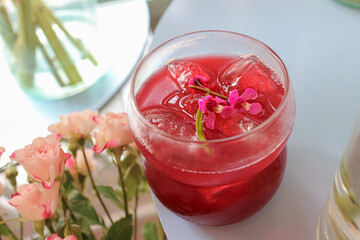 Refreshing iced Earl Grey tea with mixed berries in a clear glass, decorated with pink flowers, summer healthy drink concept in a modern cafe atmosphere.