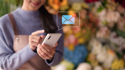 Professional retail entrepreneur using smartphone checking urgent new email communication within a busy flower shop setting