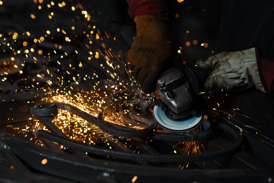 Intense sparks fly off the angle grinder as a worker shapes a custom wrought iron piece in a dramatic close-up view.