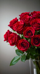 Fototapeta premium Red roses arranged in a vase with green leaves on a neutral background 
