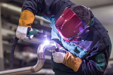 Close-up of a welder working on a metal pipe with protective gear in a workshop