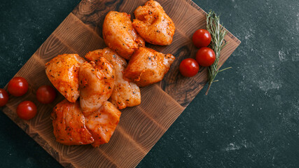 Marinated chicken pieces with tomatoes and rosemary on a wooden board.