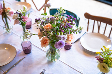 A beautifully decorated wedding or celebration event table with colorful flowers, vintage plates, and cutlery in soft natural light.The space blends modern, rustic,retro elements with charming chairs.
