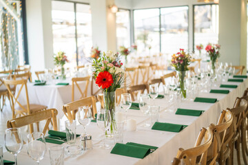 A beautifully decorated wedding or celebration event table with colorful flowers, vintage plates, and cutlery in soft natural light.The space blends modern, rustic,retro elements with charming chairs.