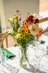 A beautifully decorated wedding or celebration event table with colorful flowers, vintage plates, and cutlery in soft natural light.The space blends modern, rustic,retro elements with charming chairs.