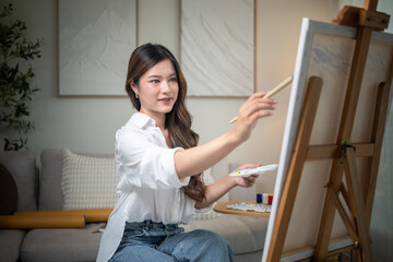 Female artist holding a palette and brush, working on her artwork at home.