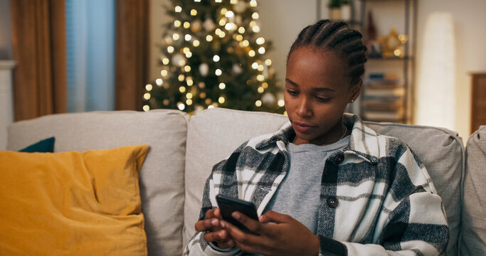 A young woman of multi-racial background sits on a couch on a winter evening. After her phone rings, she answers, talks emotionally, and gestures with her hands after learning of a terrible event. - Powered by Adobe