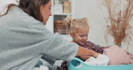 In a cozy bathroom, a little girl with blue eyes pulls out a sweatshirt from the clothes dryer and...