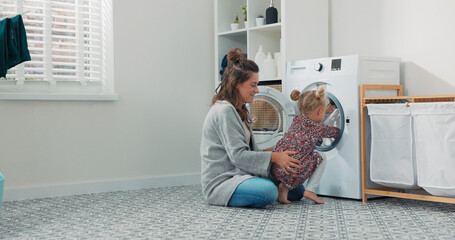 A mother shows her daughter how to operate the washer during their time together at home, enjoying...