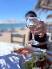 Cheers with white wine at a beachside taverna in Greece with Greek salad in foreground