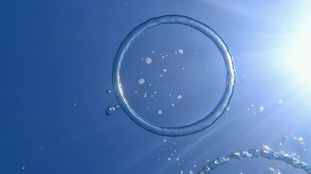 Air bubble ring under water. The freediver releases oxygen into the surface of the water in the shape of a ring. Beautiful water background with sun glare and air bubbles. Ring Bubble.