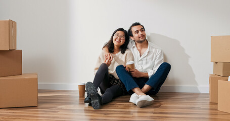 A couple enjoys coffee together in their new apartment. They sit by the wall, discussing appliances, colors, and future flat arrangements.