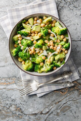 Vegan salad with broccoli, chickpeas, avocado, onions, and herbs close-up in a bowl on the table. Vertical top view from above