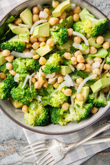 vegetable salad of broccoli, chickpeas, avocado, onion, and parsley with a spicy dressing, close-up, in a bowl on a table. Vertical top view from above