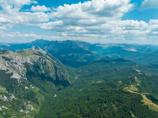 Aerial view of a mountain range with forests and a valley under a sky with clouds The scene captures a remote natural landscape
