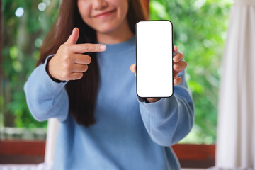 Mockup image of a woman holding and pointing finger at a mobile phone with blank white screen at...