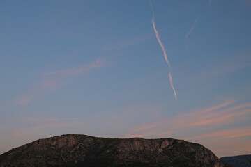 A mountain sits under a sky with vapor trails The sky is blue and has orange and pink streaks The time of day appears to be near sunset or sunrise