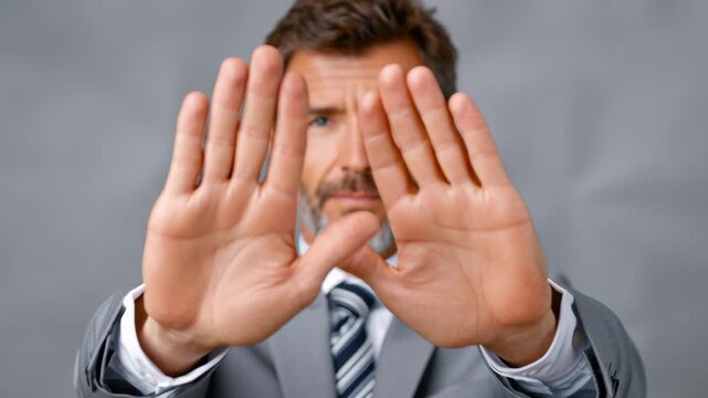 Businessman in gray suit extends hands forward, signaling a stop gesture, showcasing determination and authority in a professional setting, emphasizing clear communication and assertiveness in action