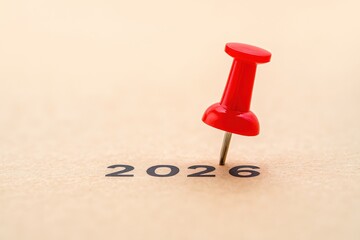 Marking 2026 with a red pushpin on a tan surface, symbolizing a future date.