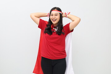Close-up photo of Indonesian woman celebrating Indonesian independence while tying a red and white ribbon on her head facing the camera while smiling.